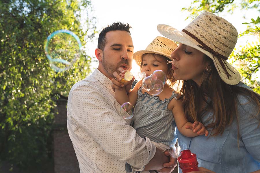 Personal Insurance - Parents Blowing Bubbles with Their Young Daughter Outside on Warm Summer Day